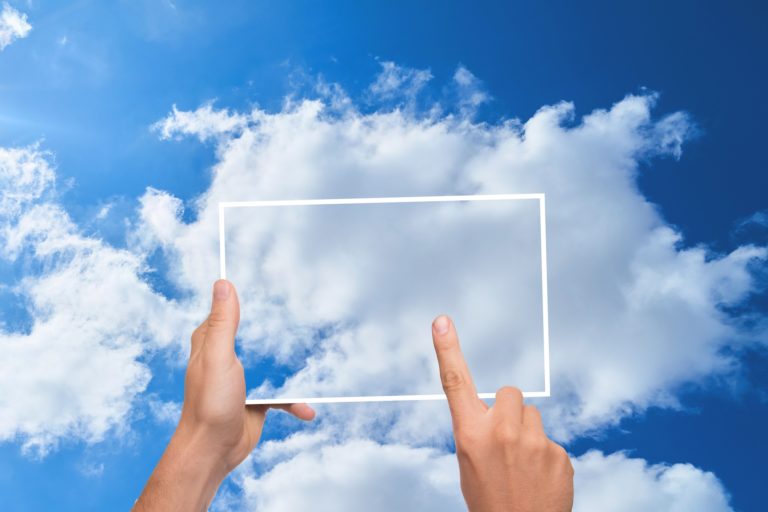 Manos sosteniendo una pantalla transparente contra un cielo con nubes